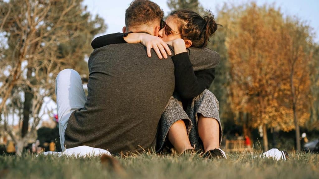 A couple sitting on the grass outdoors hugging closely.