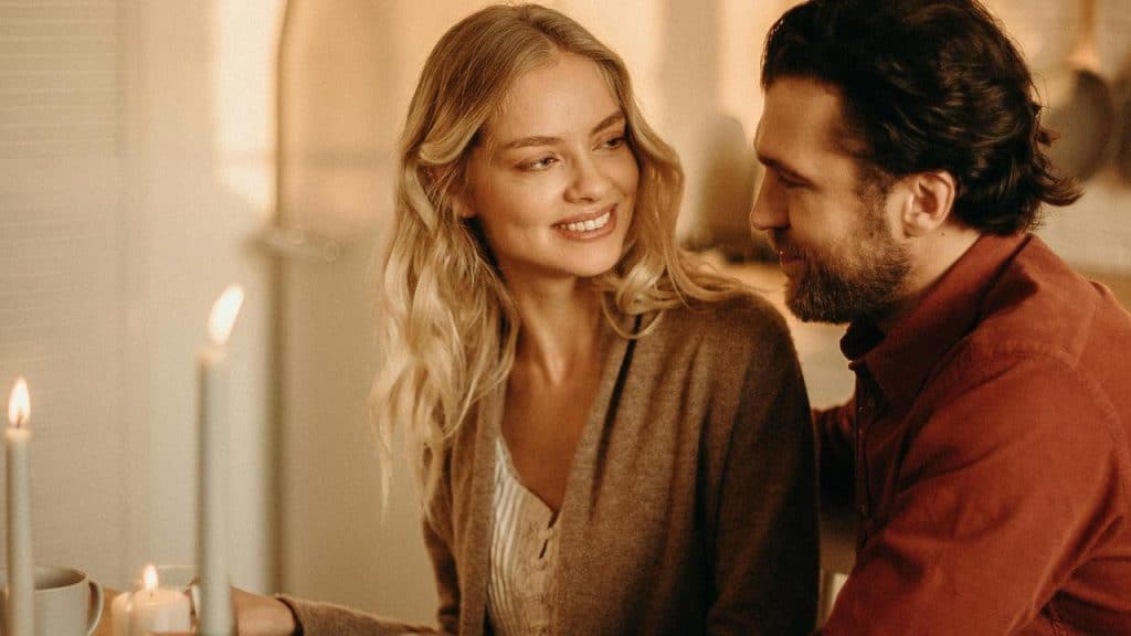 A couple sitting together at a candlelit table, smiling at each other warmly.