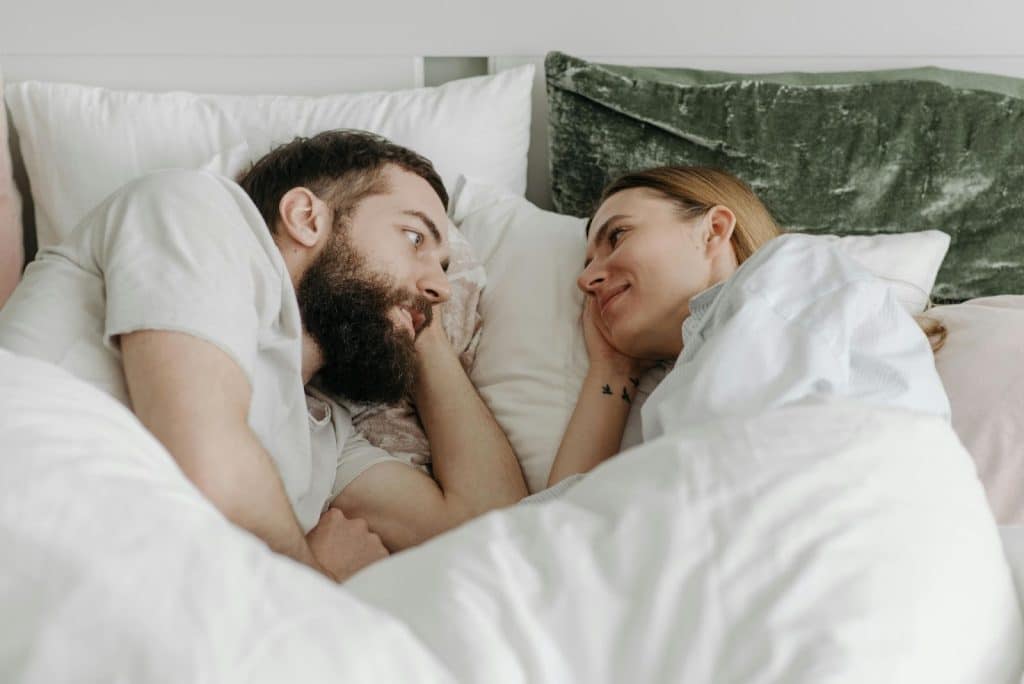 A man and woman facing each other while laying on bed