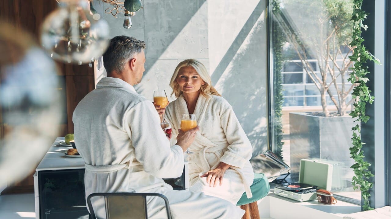 A mature couple having mimosas in bathrobes.