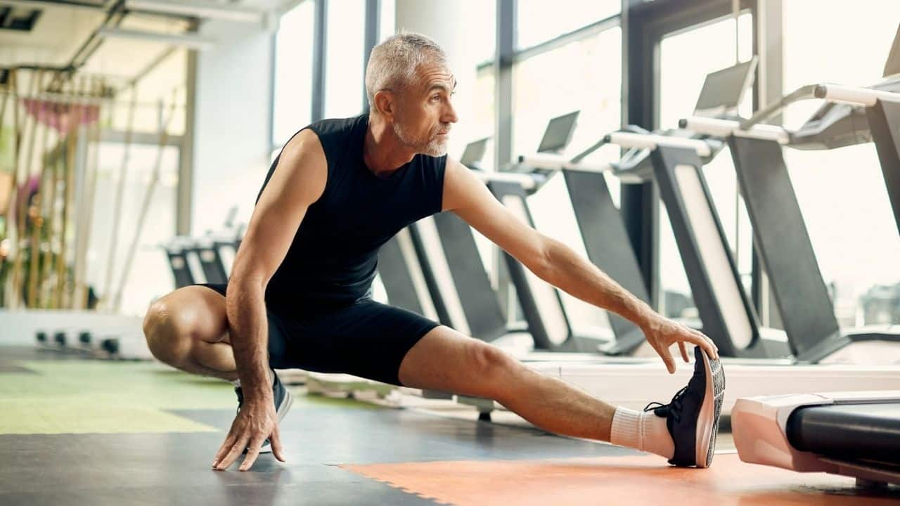 A focused, middle-aged man stretches his leg at a gym.