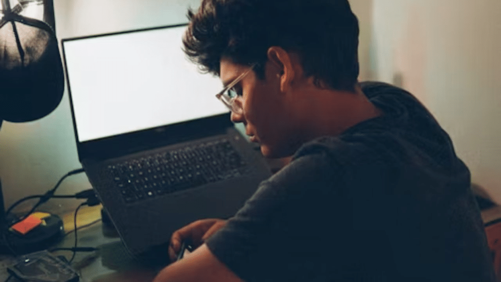 Man with a blank stare browsing aimlessly on his cellphone with laptop on the side