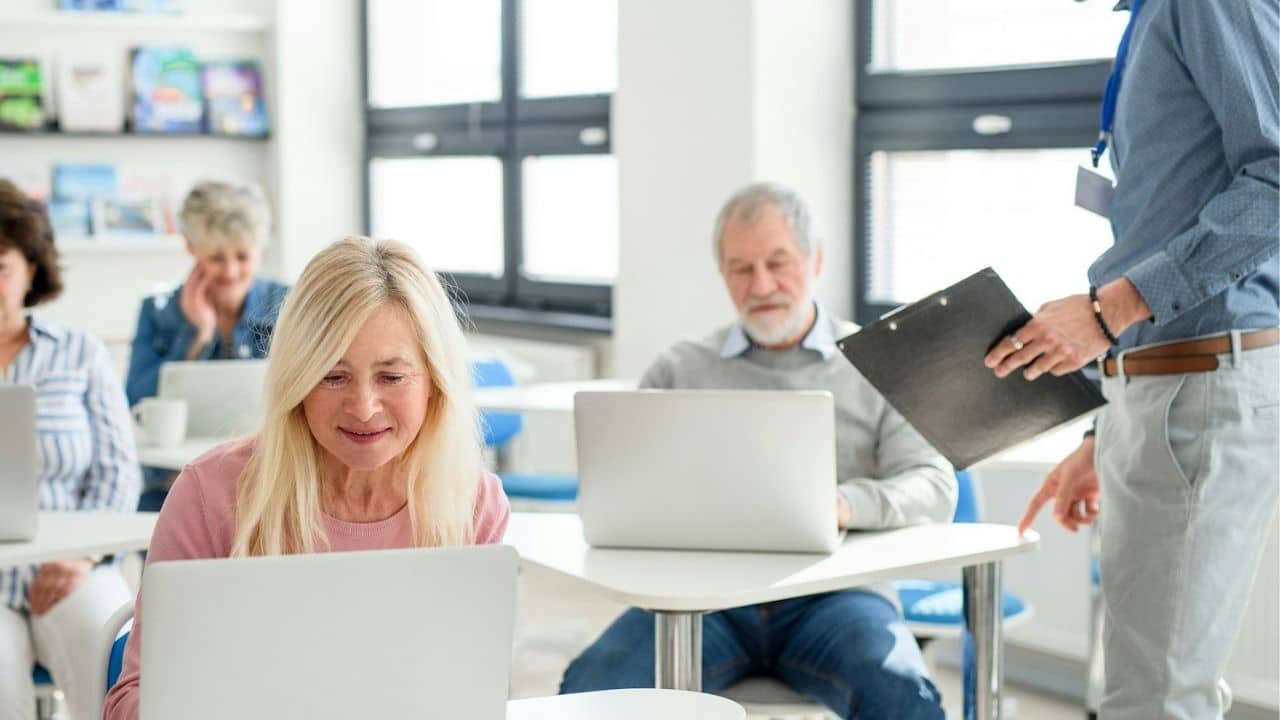A classroom of senior students learning to use laptops from a teacher.