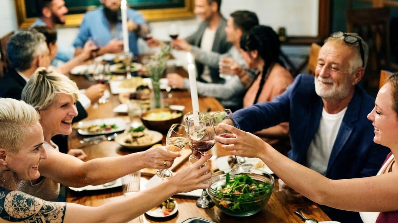 A lively group of diverse people gathered at a dinner table toasting with wine glasses.