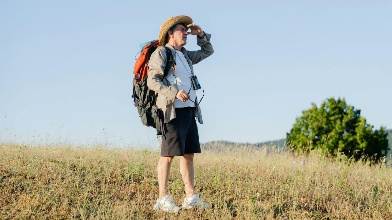 A mature man wearing a hat and a backpack looks out at the horizon.