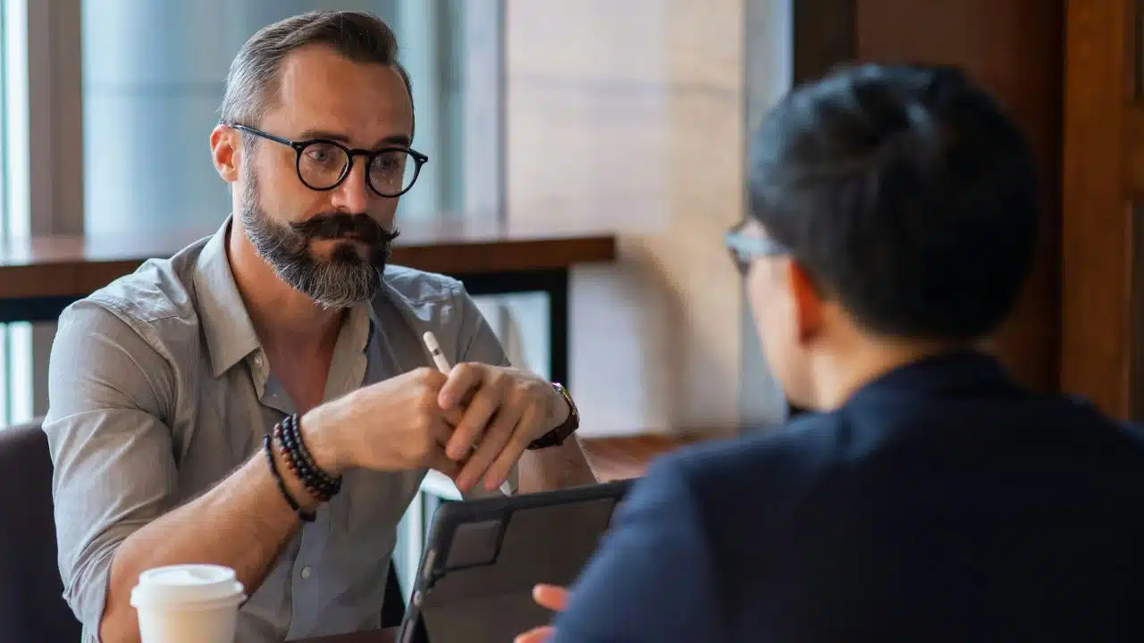 A businessman with glasses and a beard is in a serious conversation with another person.