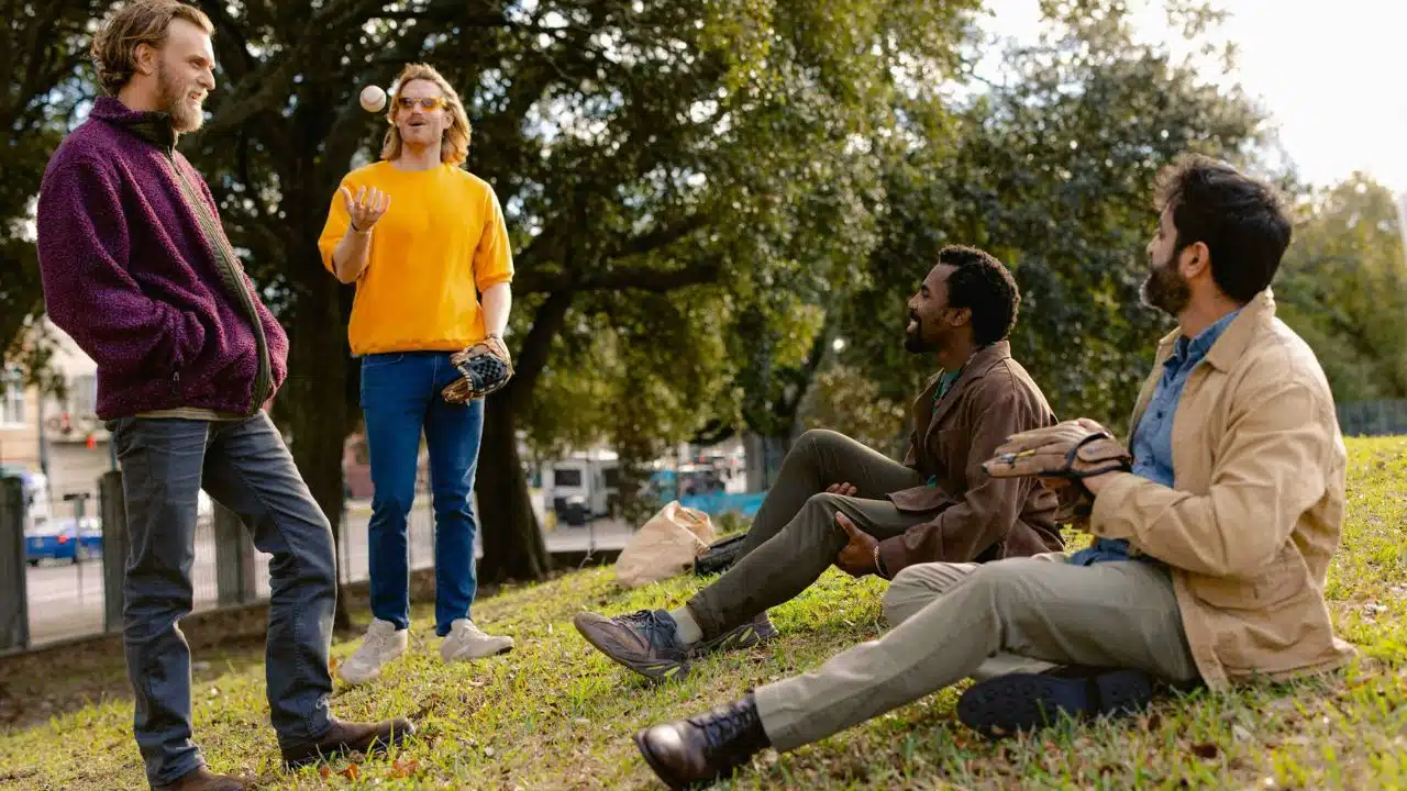 A group of four diverse men are playing with a baseball in a park.