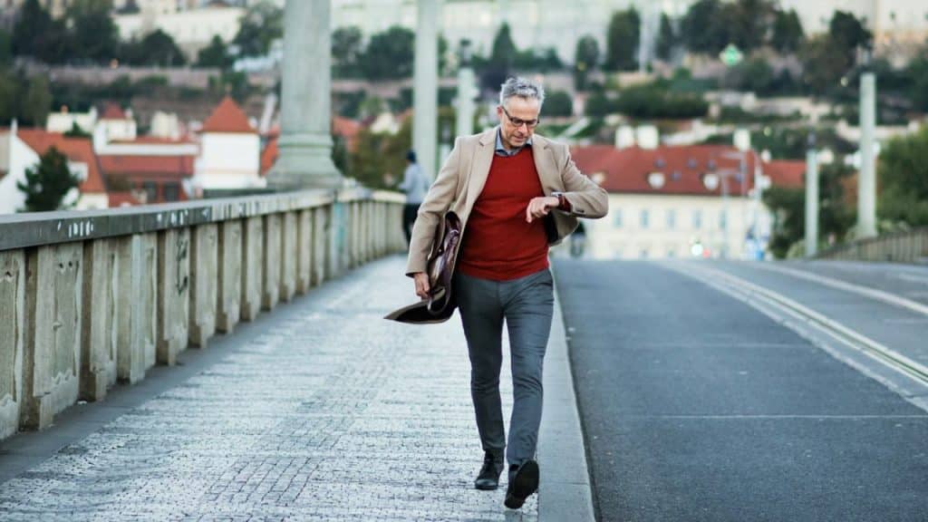 A businessman looks at his watch as he quickly walks along a bridge, holding a briefcase.