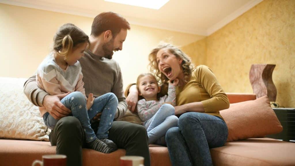 A joyful family of four is sitting on a sofa and laughing together.