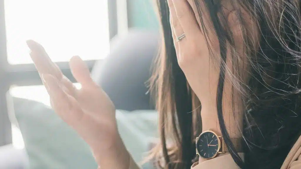 A woman covering her face with her hand while wearing a watch and ring.