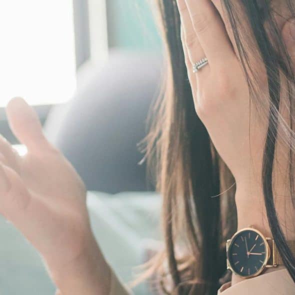 A woman covering her face with her hand while wearing a watch and ring.
