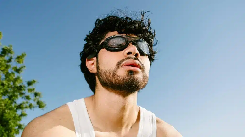 A man wearing fogged-up goggles and a white tank top under a clear blue sky.