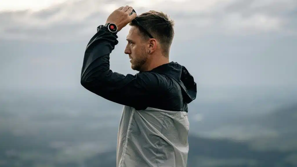 A man in a jacket adjusting his headwear outdoors.