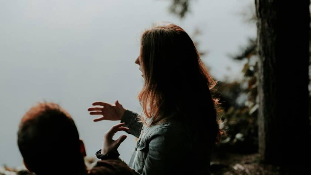 A woman gesturing while talking to someone outdoors.