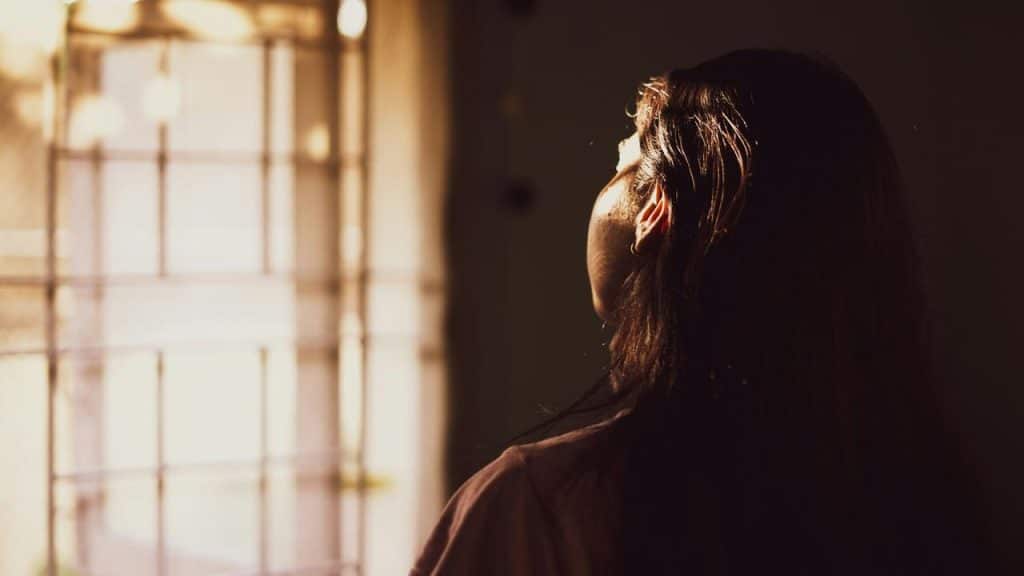 A woman looking out a window with sunlight shining on her face.