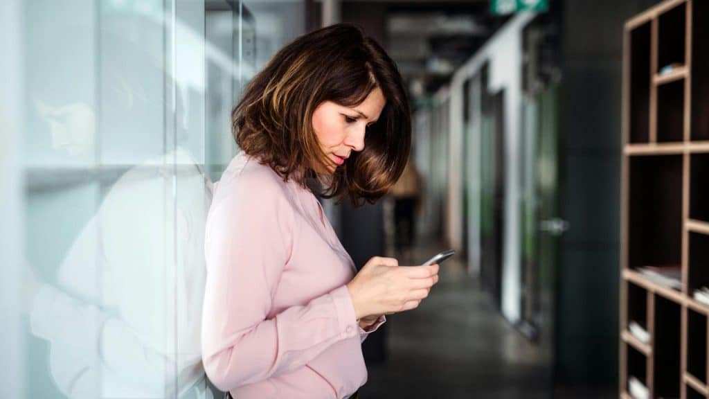 A woman standing in a hallway looking at her phone.