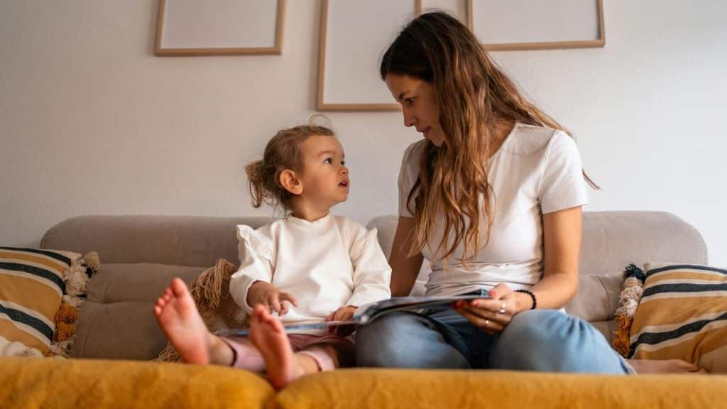 A mother and child sitting on a couch reading a book together.