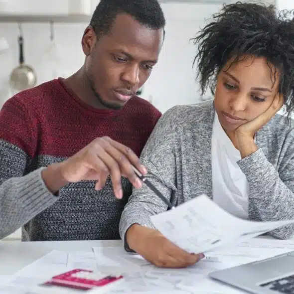 A couple reviewing financial documents together at a kitchen table with a laptop.