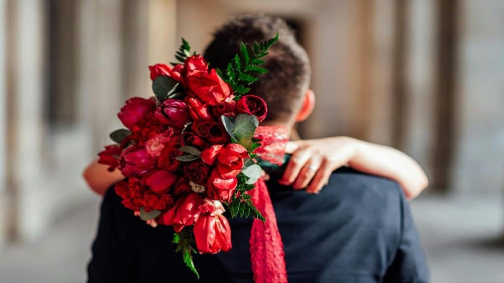 A couple hugging while a woman holds a bouquet