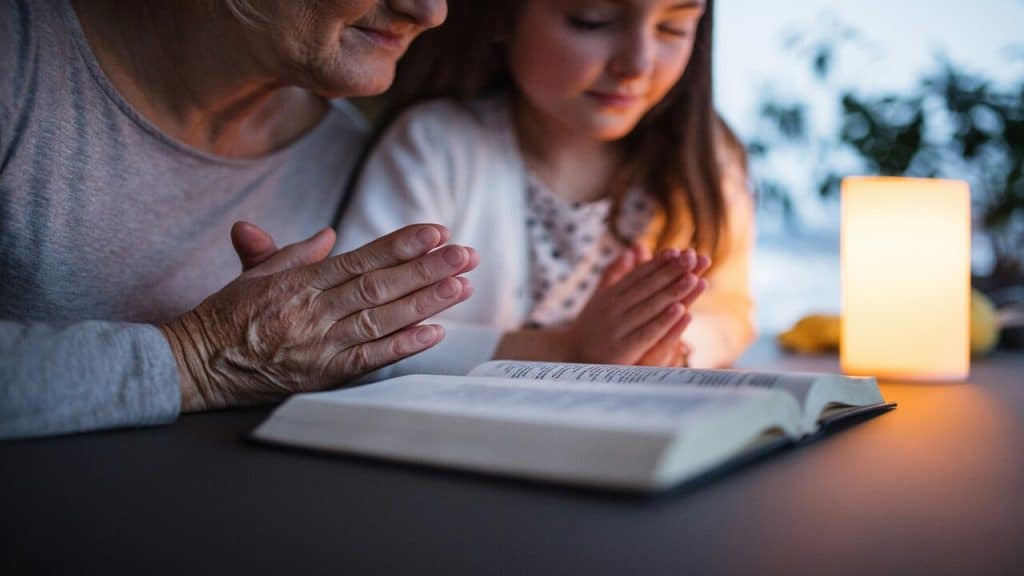 A grandma teaching her granddaughter how to pray.