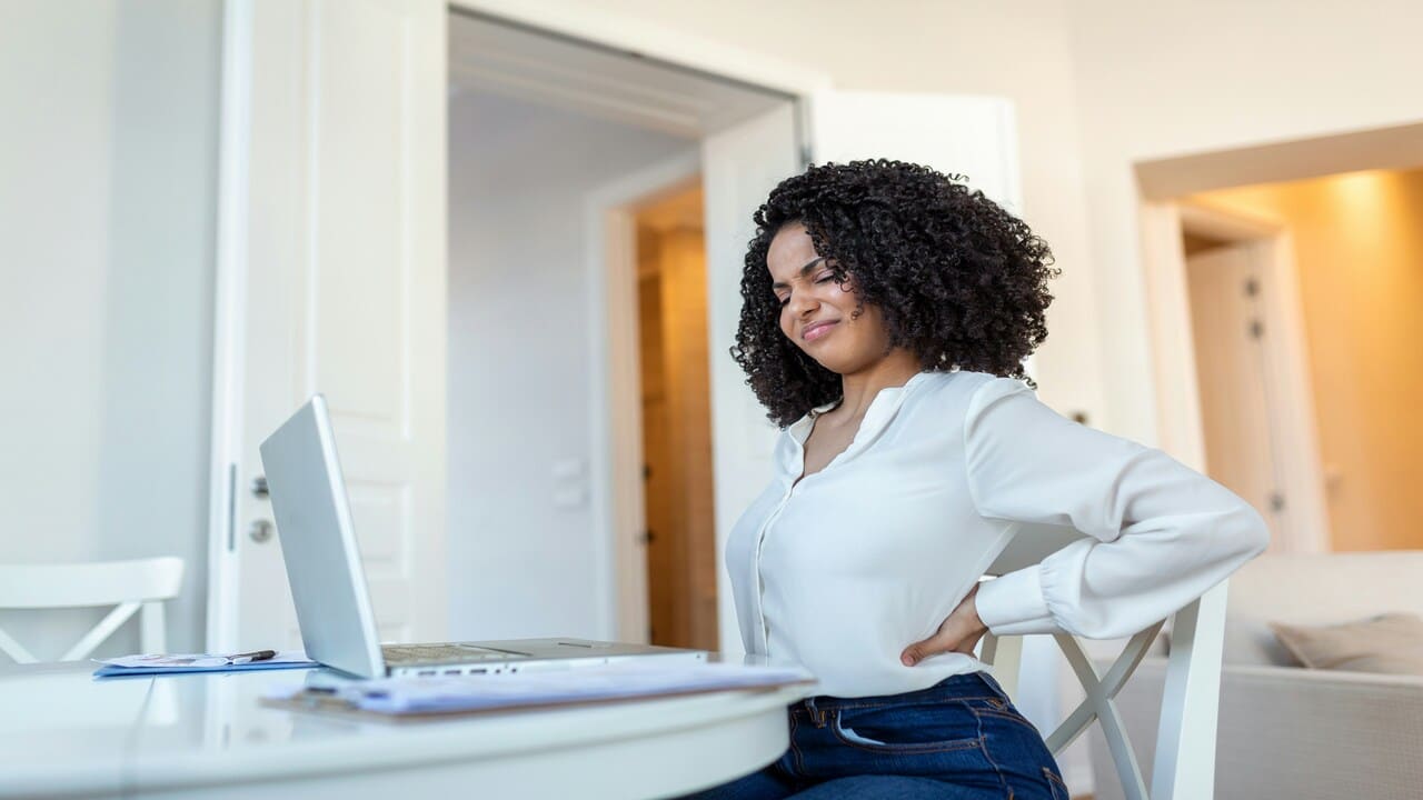 A woman clutching at her back at work.