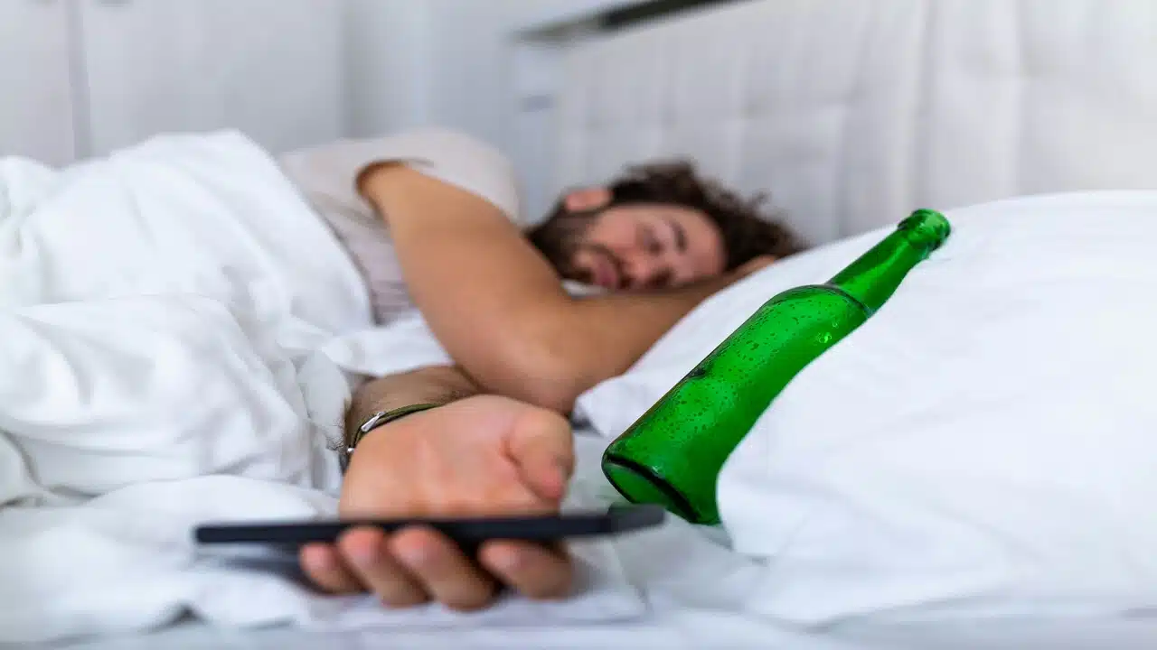 A drunk man with an alcohol bottle in bed.