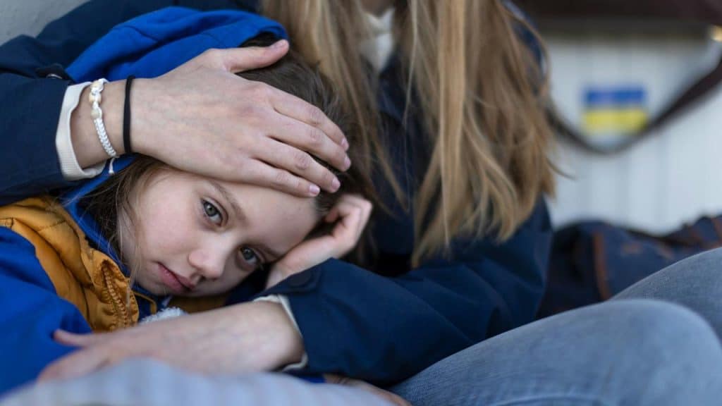 A child resting on a woman’s lap while being comforted with a hand on the head.