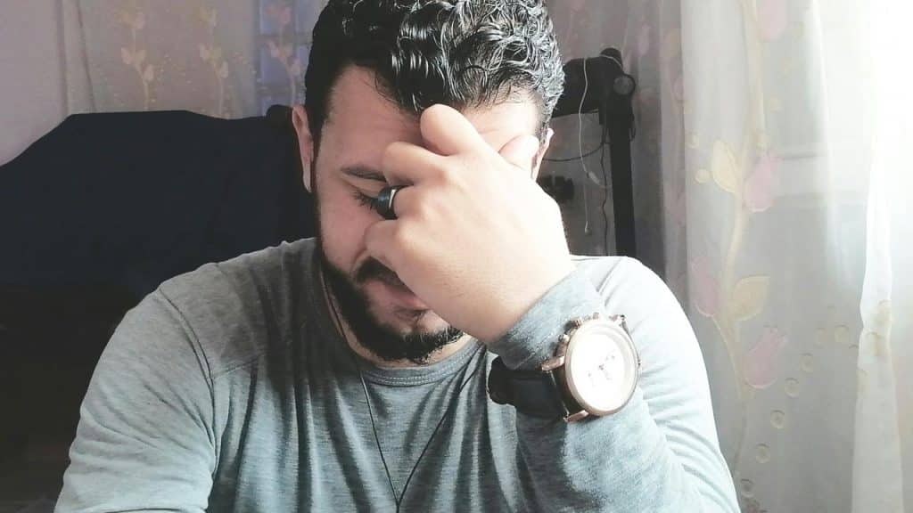 A man sitting indoors with his hand on his forehead looking stressed.