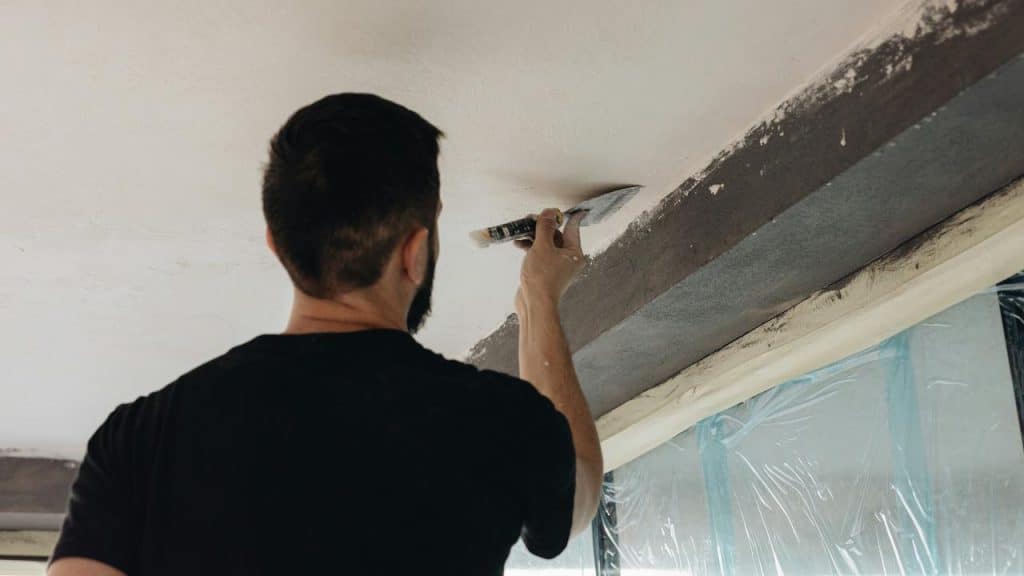 A man plastering a ceiling with a trowel during renovation work.