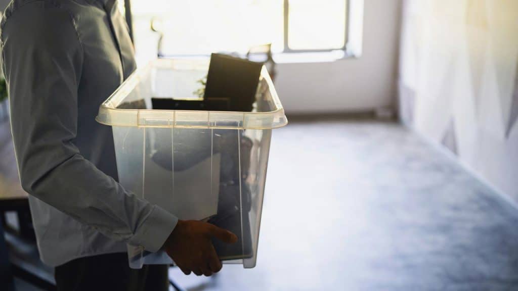 A person carrying a clear plastic box filled with office belongings.