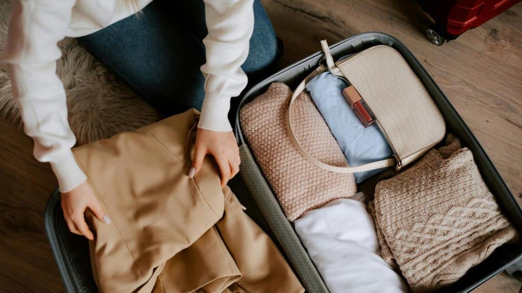 A person packing clothes and a bag into a suitcase.