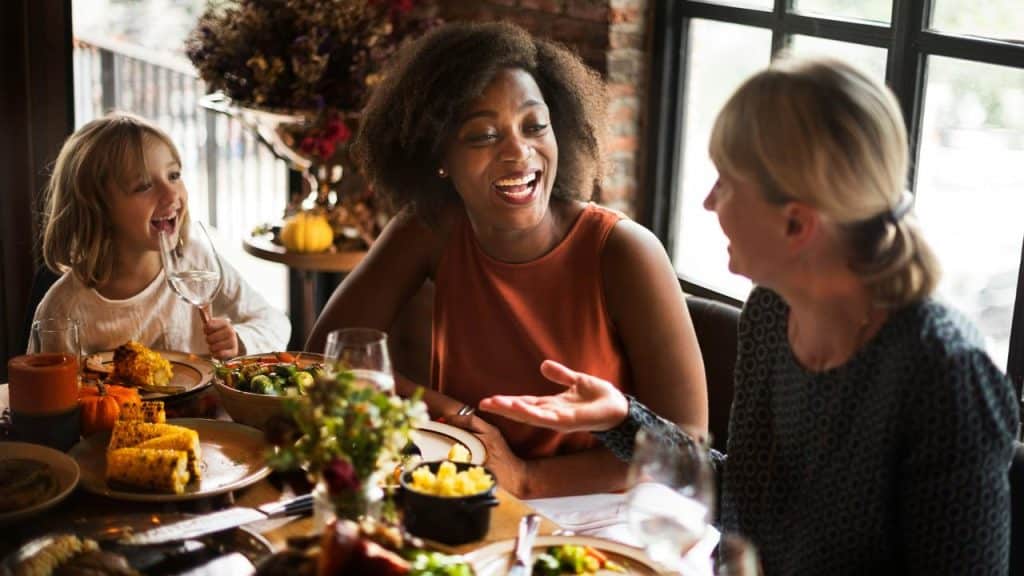 A group of people smiling and talking while sharing a meal at a table.