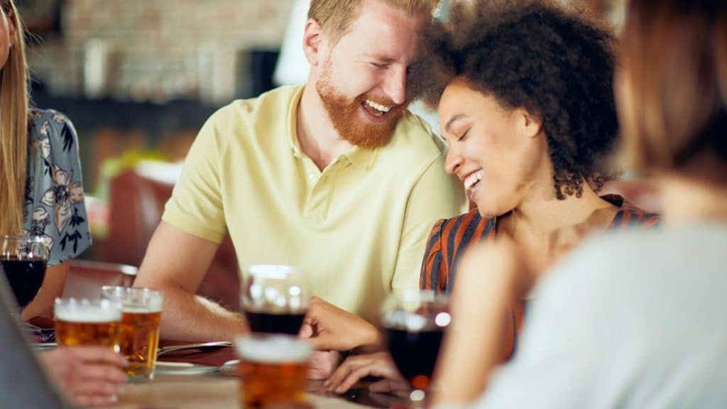 A couple laughing and enjoying drinks with friends at a table.