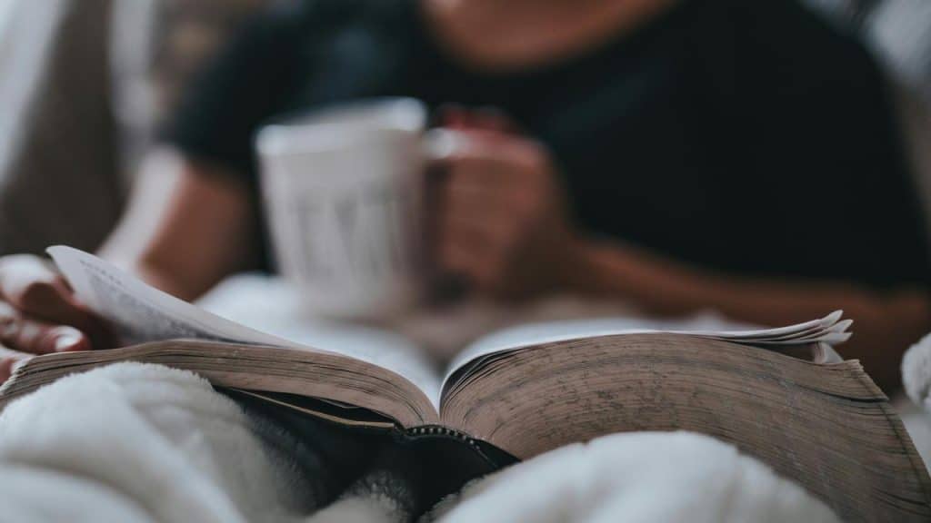A person reading a book while holding a mug.