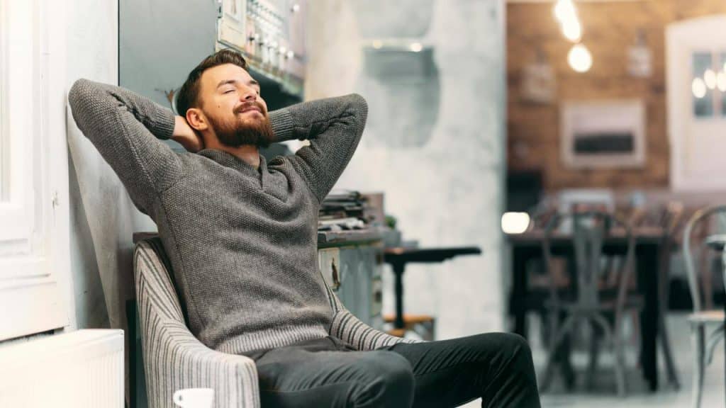 A man relaxing in a chair with his hands behind his head and eyes closed.