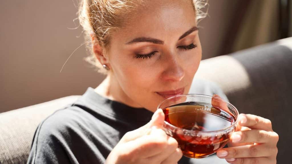 A woman enjoying a cup of tea with her eyes closed.