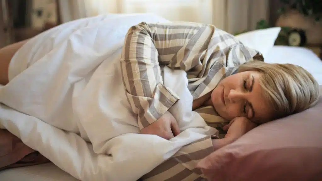 A woman sleeping peacefully in bed with striped pajamas.