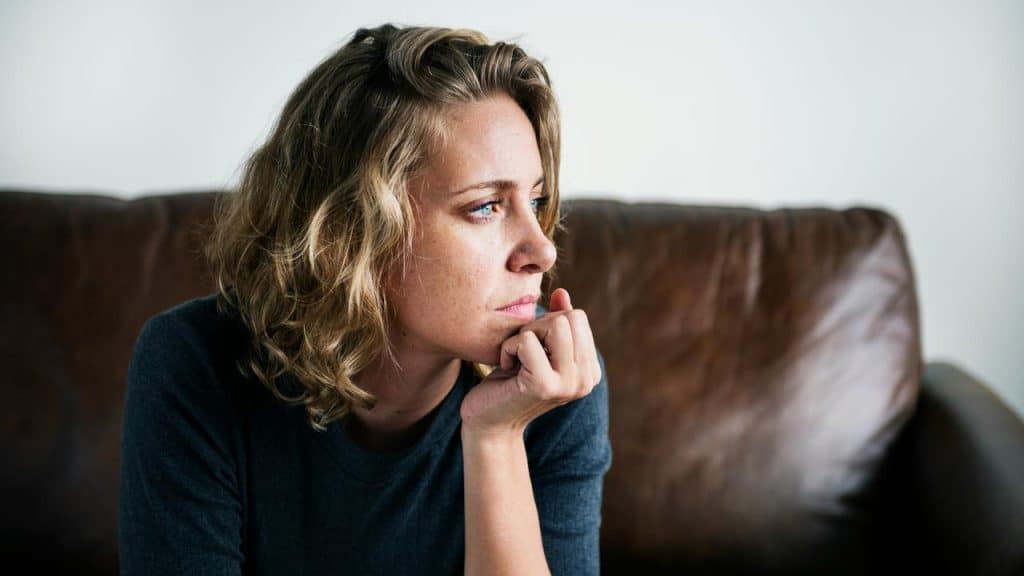 A woman sitting on a couch looking thoughtful and pensive.