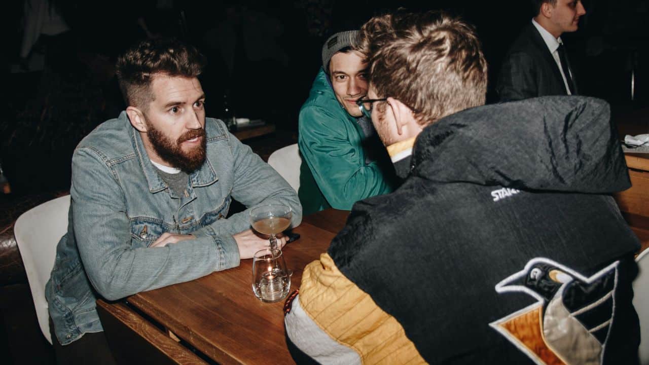 Three men are seated at a dimly lit bar, engrossed in conversation.