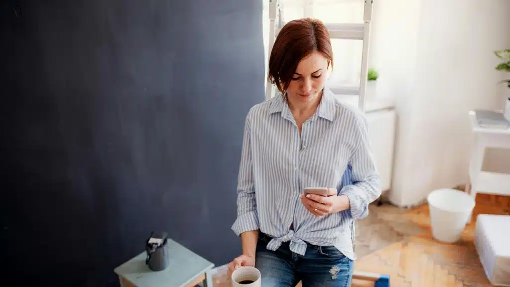 A woman holding a coffee cup while looking at her phone.