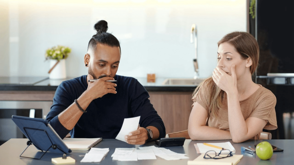 A man and woman look stressed while working on paperwork at a table.