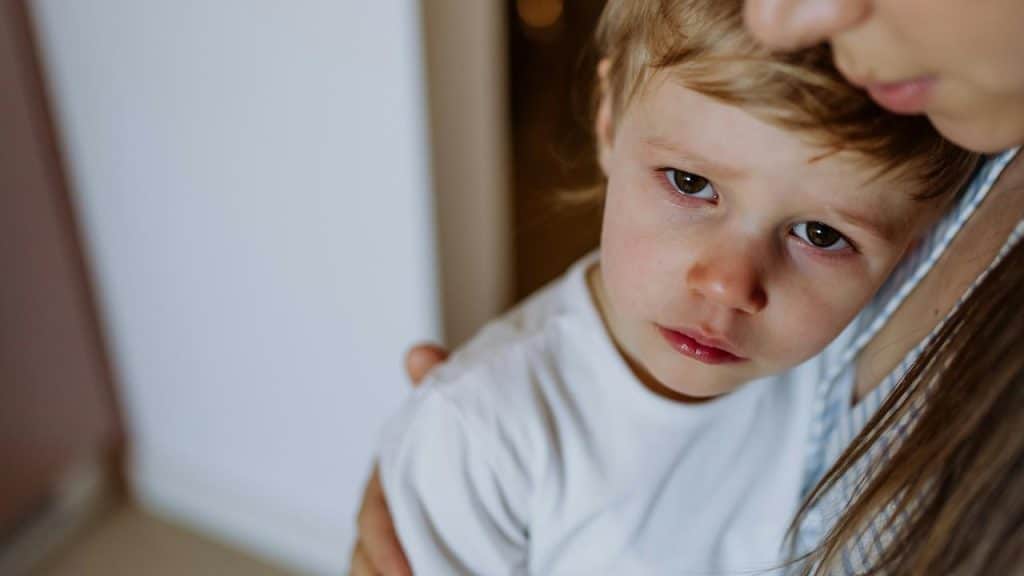 A young boy looking sad while his mother hugs him.