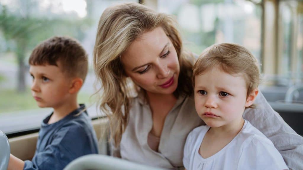 A mother with her two children riding the bus, appearing to console the other child.