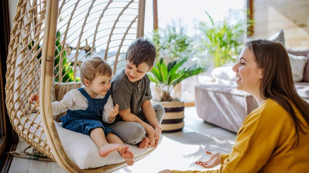 A happy mother looking after her two children on a hanging chair.