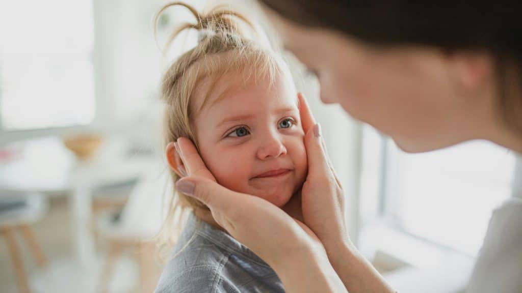 A mother tenderly holding her daughterโs cheeks with both hands.