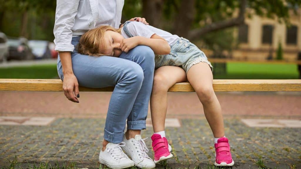 A child leaning comfortably into her motherโs lap with her eyes closed.