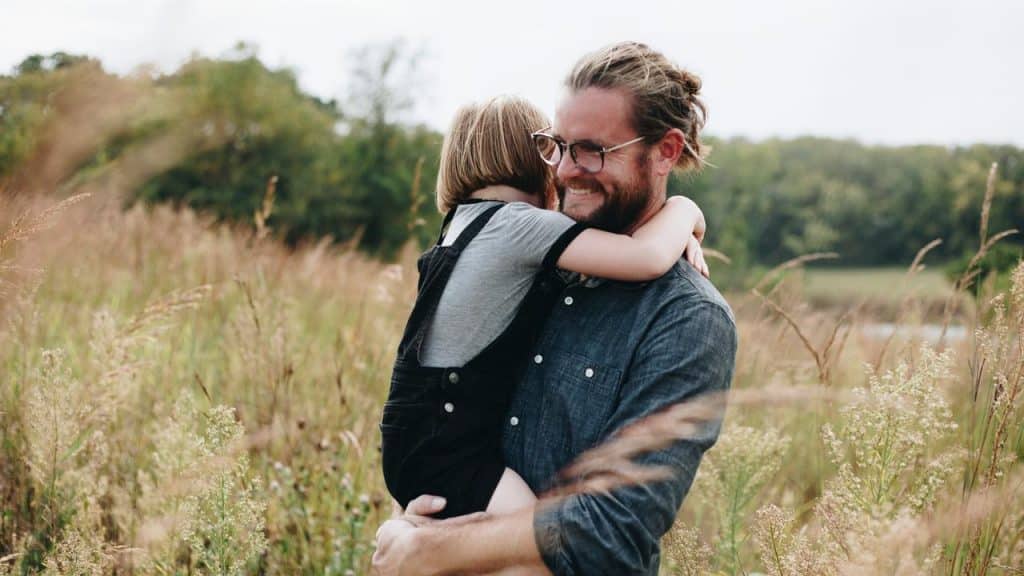 A father happily carrying his daughter out on a grass field.