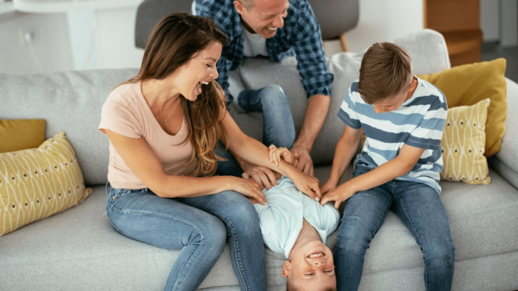 A joyful family is playing and laughing together on a gray couch.