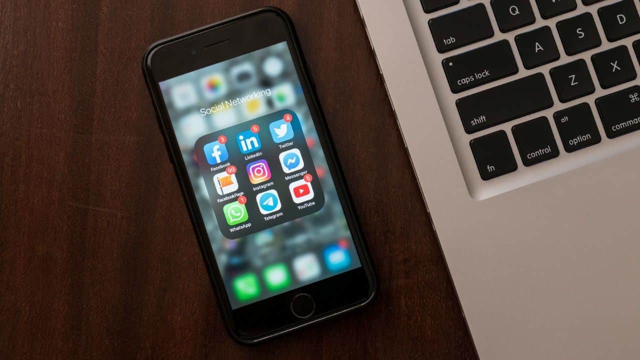 A cell phone displays a folder of social media apps next to a laptop keyboard.