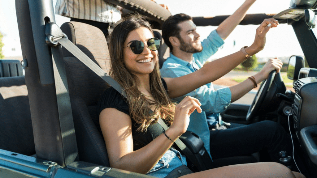 A happy young woman in sunglasses smiles as she rides in a convertible with friends.
